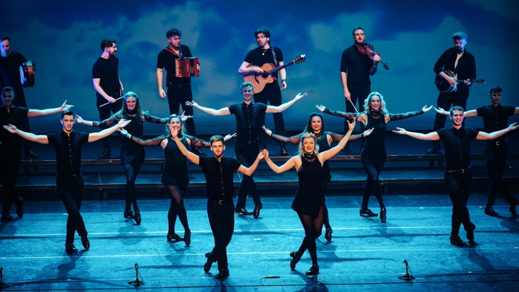 Irske dansere på en scene med lys og musikere bagved