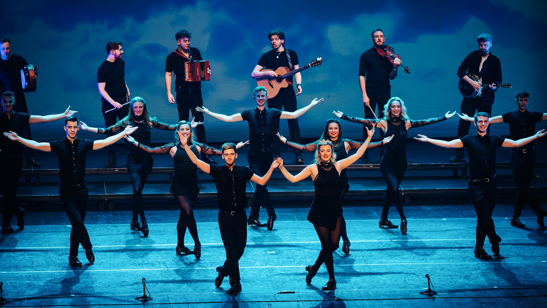 Irske dansere på en scene med lys og musikere bagved