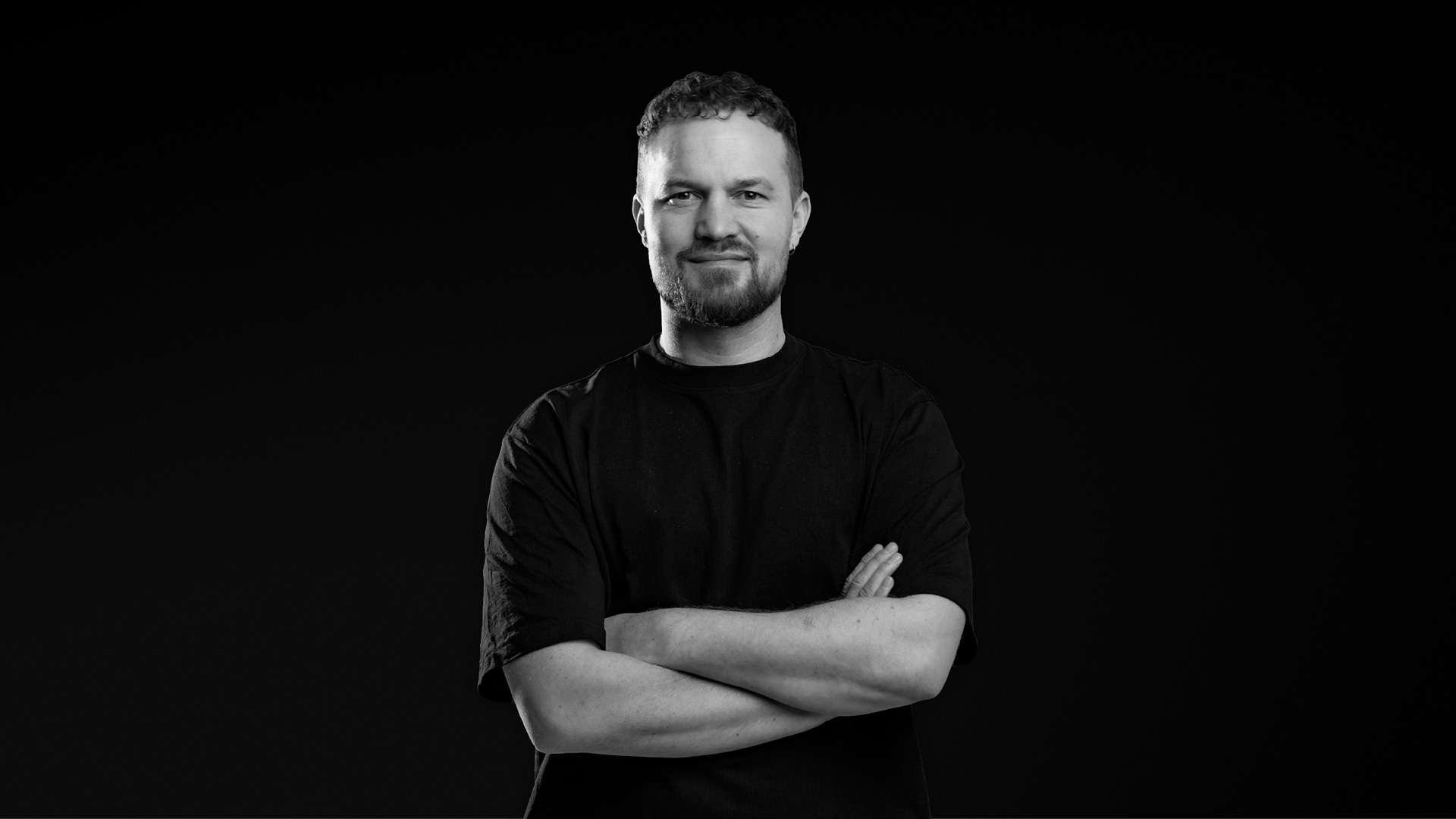 Den mandlige komiker Troels Messmann kigger ind i kameraet med armene over kors